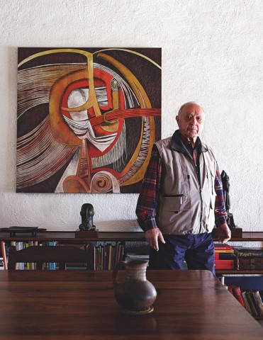 Click the image for a view of: Egon Guenther stands next to a Cecil Skotnes wood panel in the wing of the house and former gallery where he lived in Johannesburg